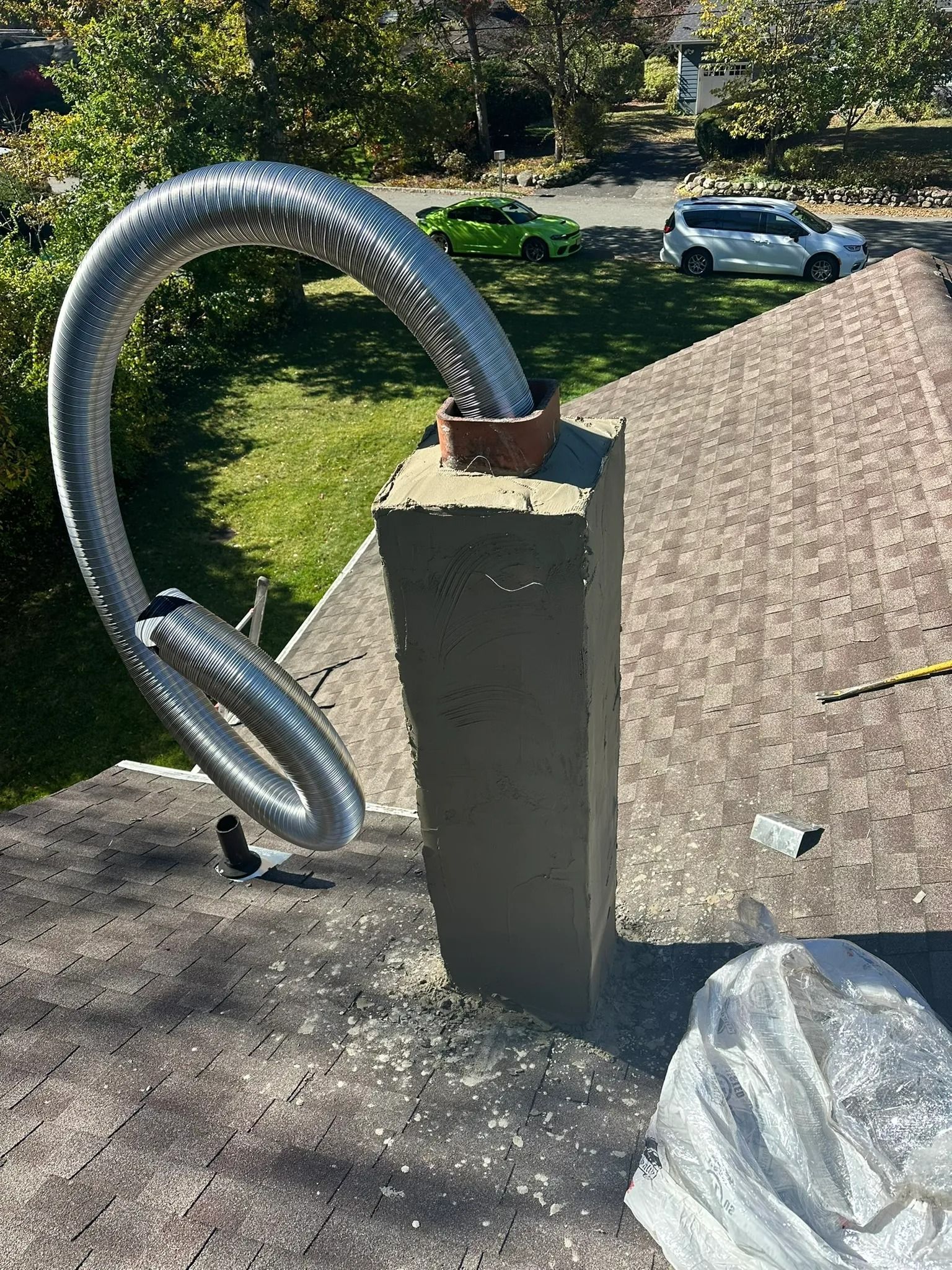 Flexible metal hose looped over a concrete post outdoors, beside a sunlit yard and gravel slope.
