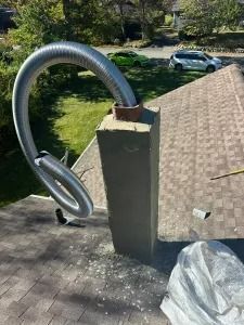 Coiled silver ducting attached to a rooftop chimney, with a driveway and parked cars in the background