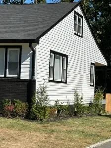 White house exterior with black trim, windows, and a small front lawn under a sunny sky