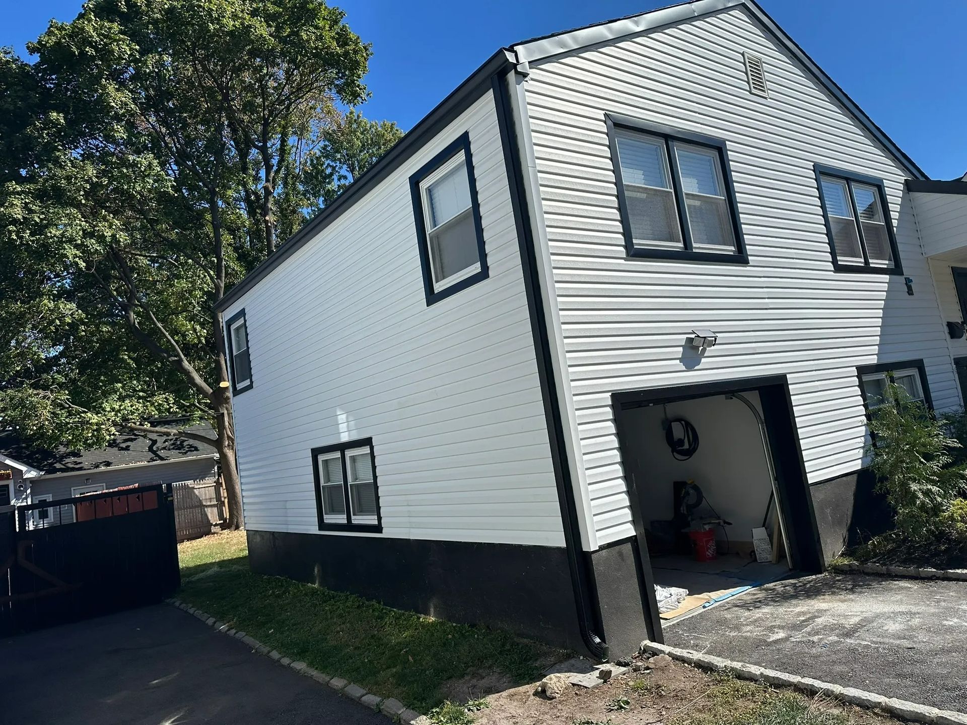 White two-story house with black trim and open garage, viewed from the driveway on a sunny day