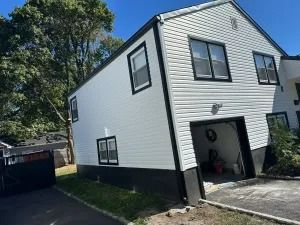 White two-story house with black trim, open garage, and driveway beside trees