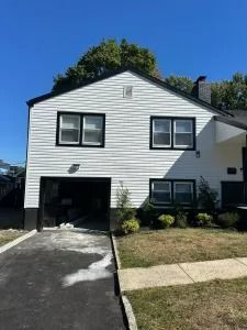 White two-story house with black trim, attached garage, driveway, and small front lawn under a blue sky