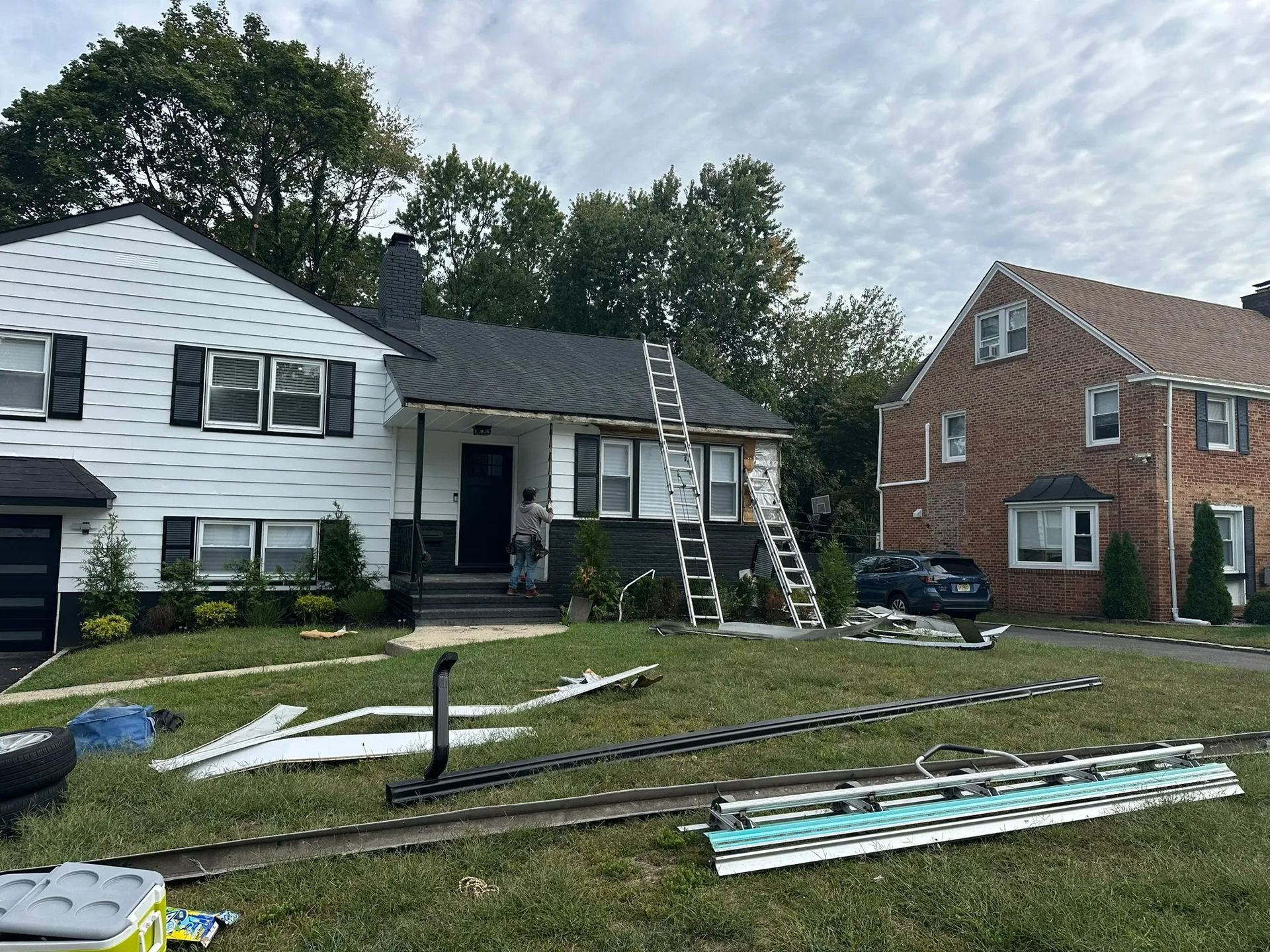 Suburban house with a ladder on the roof and debris scattered across the front lawn.