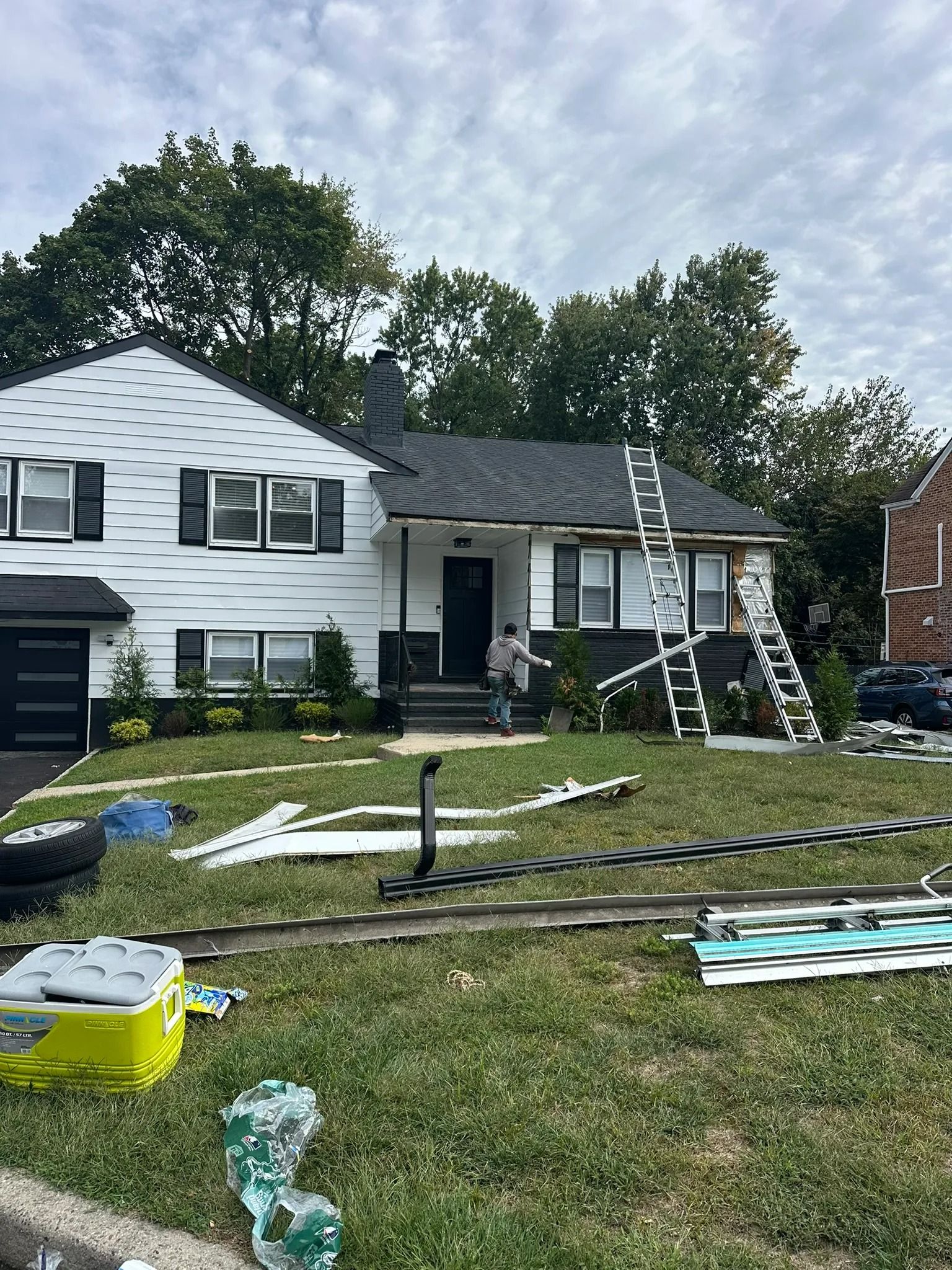 Single-story white house with porch and lawn covered in roofing materials after storm damage