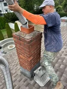 Worker inserting a metal flue into a brick chimney on a shingled roof