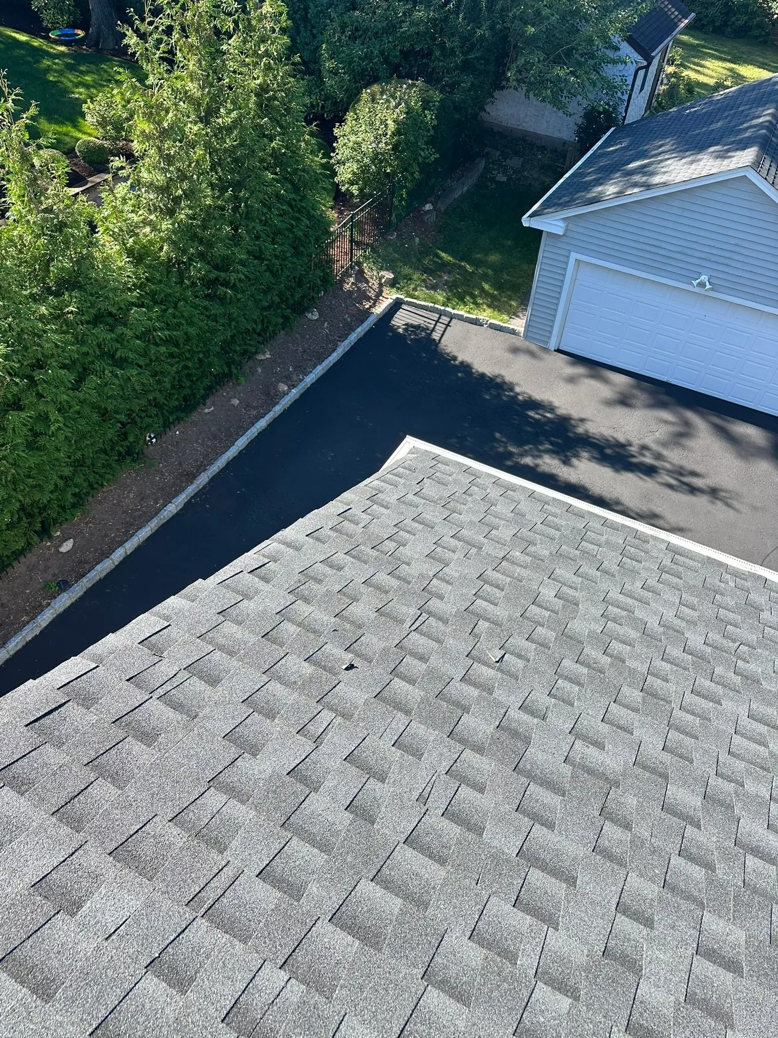 Roof with gray shingles beside a blue garage, bordered by trees and sunlight