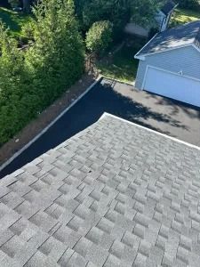 Roof shingles overlooking a driveway beside a gray garage and green trees