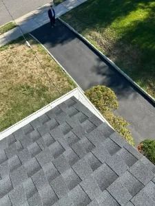 Aerial view of a driveway beside a lawn and a roof with gray shingles.