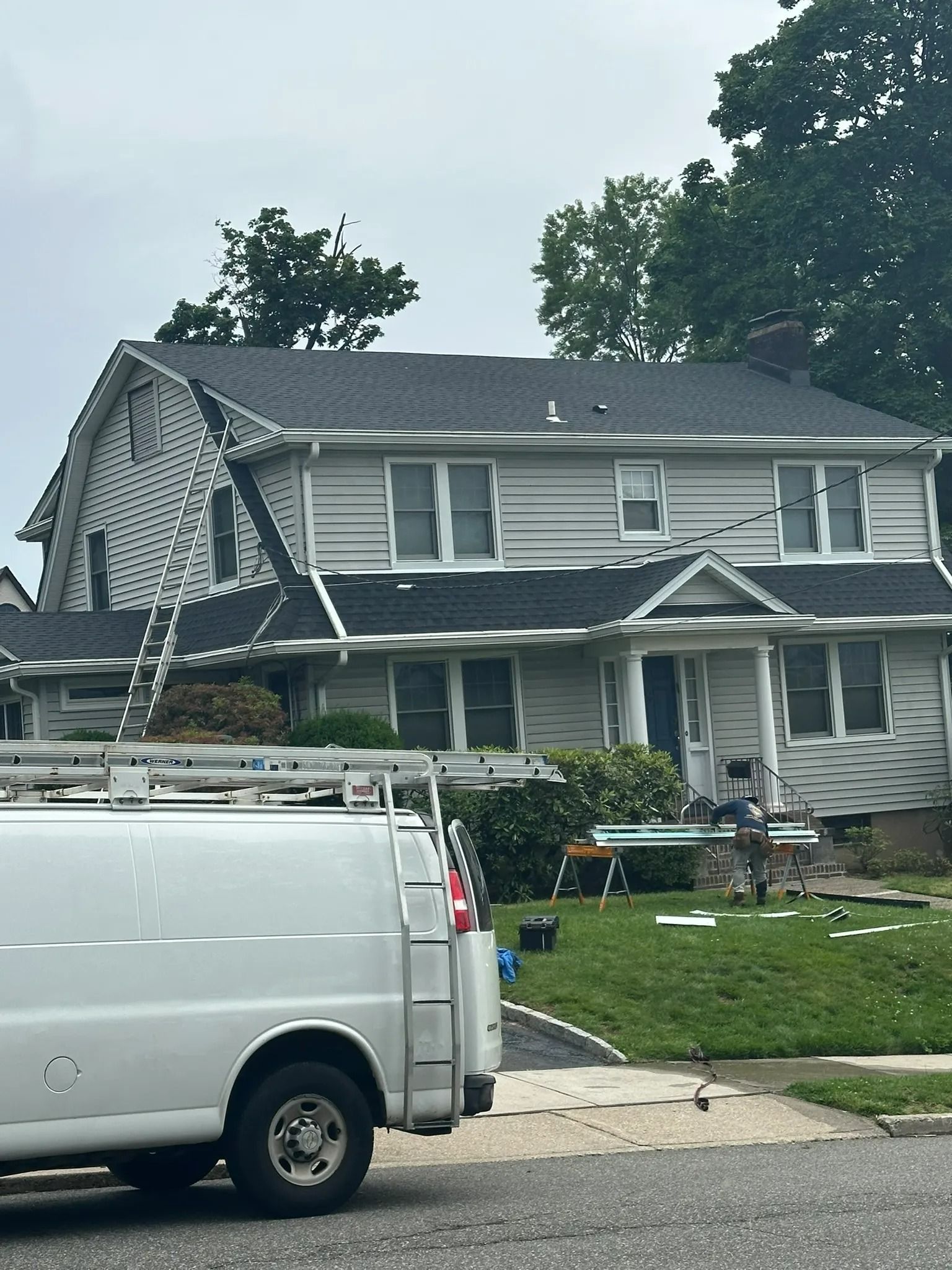 Damaged two-story gray house with a collapsed front porch and a white van parked in front