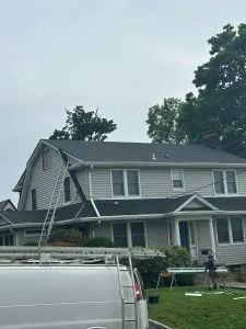 Two-story gray house with a white van parked in front and trees behind it