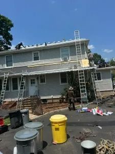 Workers with ladders painting a gray two-story house exterior under a blue sky.