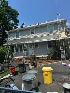 Two-story house under renovation with ladders, scaffolding, and trash bins in the driveway