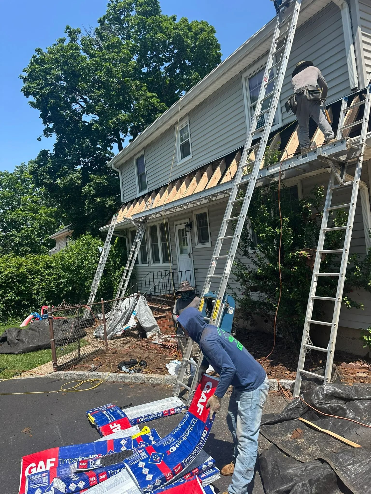 Two workers on ladders repairing house siding with ladders, tools, and debris on the ground.