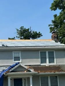 House roof under repair with blue tarp and exposed shingles under a clear sky