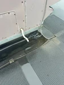 White cord hanging beside a gray metal wall and textured floor inside a train or bus aisle