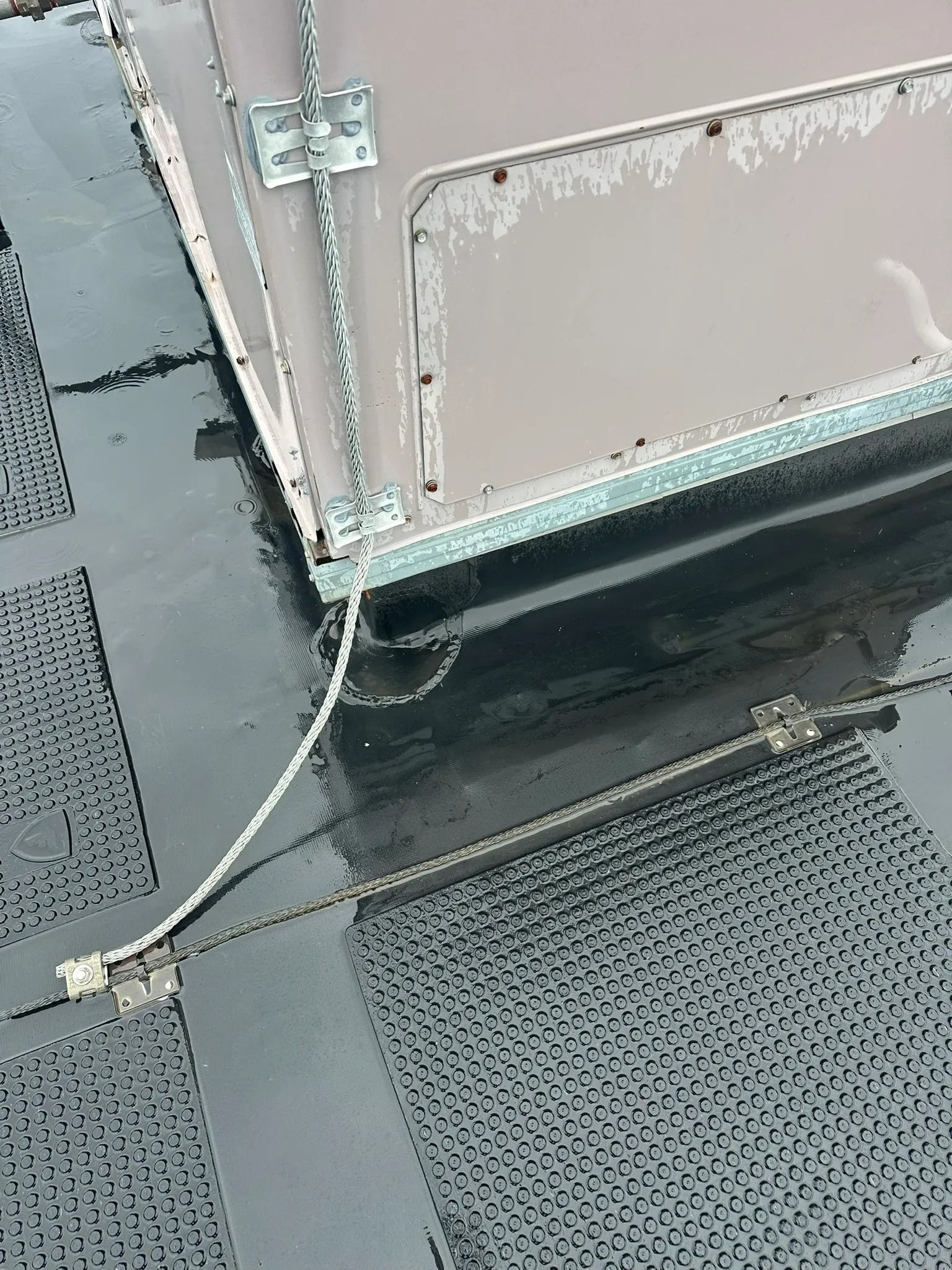 Close-up of a rooftop vent and metal flashing beside dark shingles, with a white cable running along the edge.