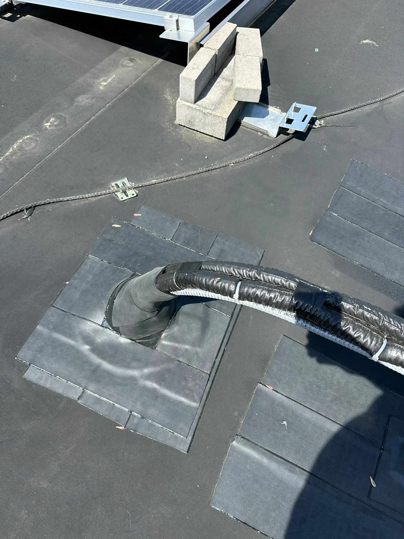 Rooftop with black roofing material, a curved cable, and cinder blocks holding down equipment.