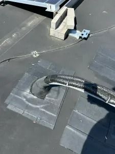 Roof vent hose exiting a black membrane roof near cinder blocks and tools