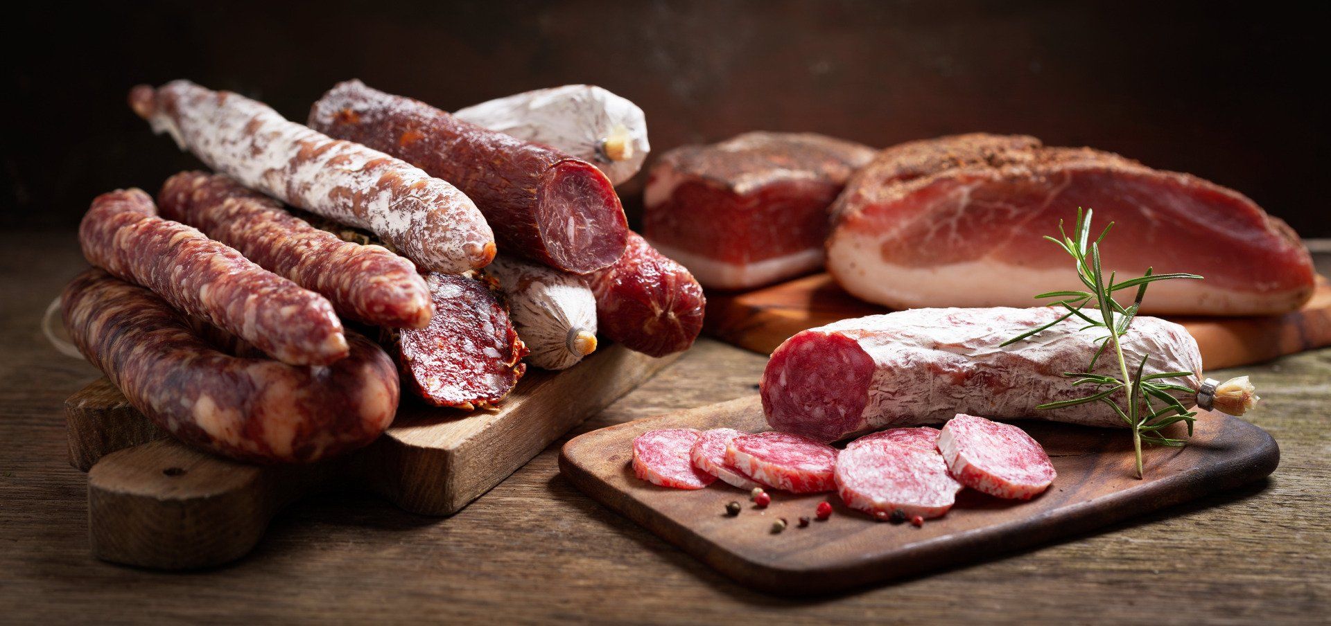 Surtido de embutidos curados y salami en rodajas sobre tablas de madera con hierbas aromáticas en un ambiente rústico.