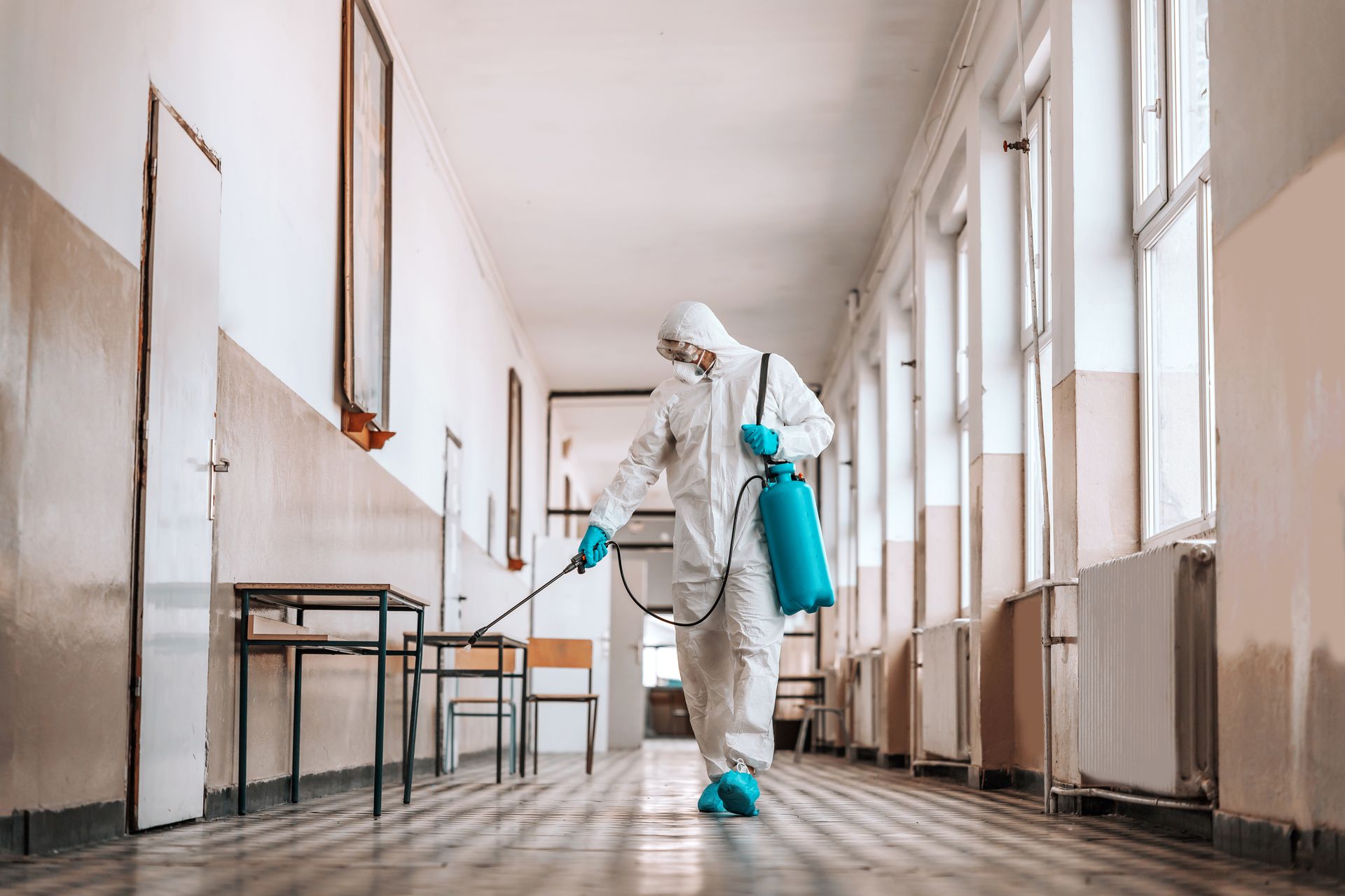 A person in a protective suit is disinfecting a hallway in a building.
