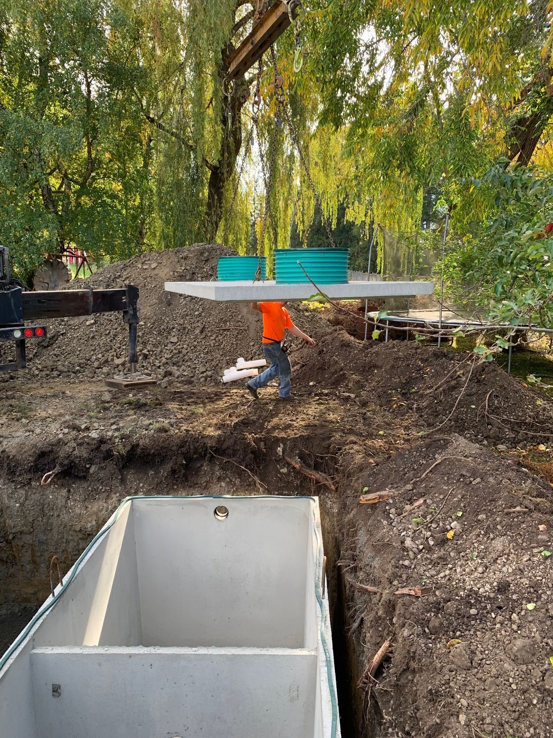 Blue pipes in a trench, leading to a gray junction box, outdoors in a hillside.