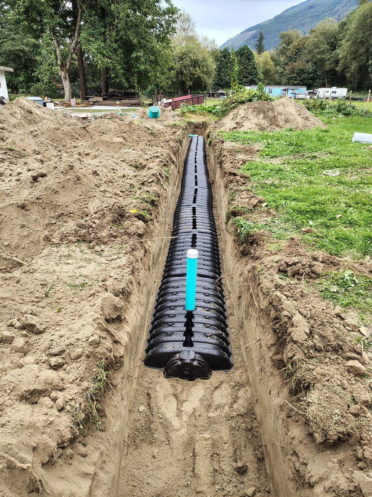 A narrow trench with black drainage pipes installed, a green PVC pipe visible.
