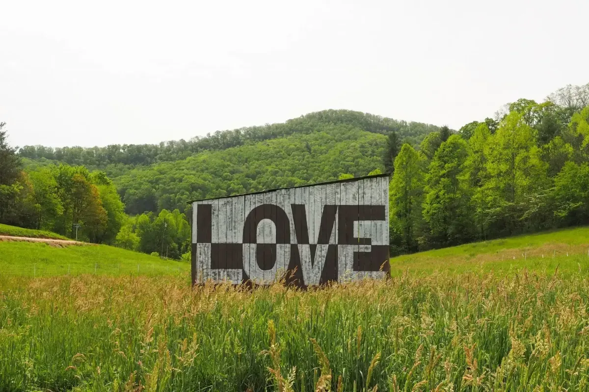 White barn on Franny's Farm with “LOVE” painted on it in a grassy field, with green hills and trees in the background.