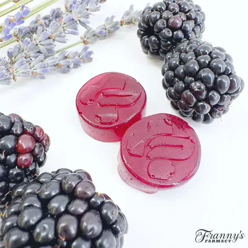 Blackberries, two red lozenges with a leaf imprint, and lavender sprigs on a white surface
