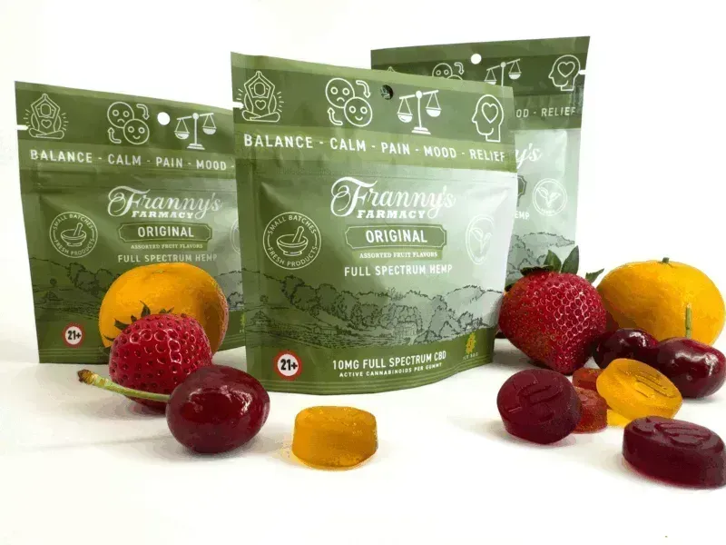 Franny's Farmacy Original CBD gummies and fruit, bags are green with white text, on white background.