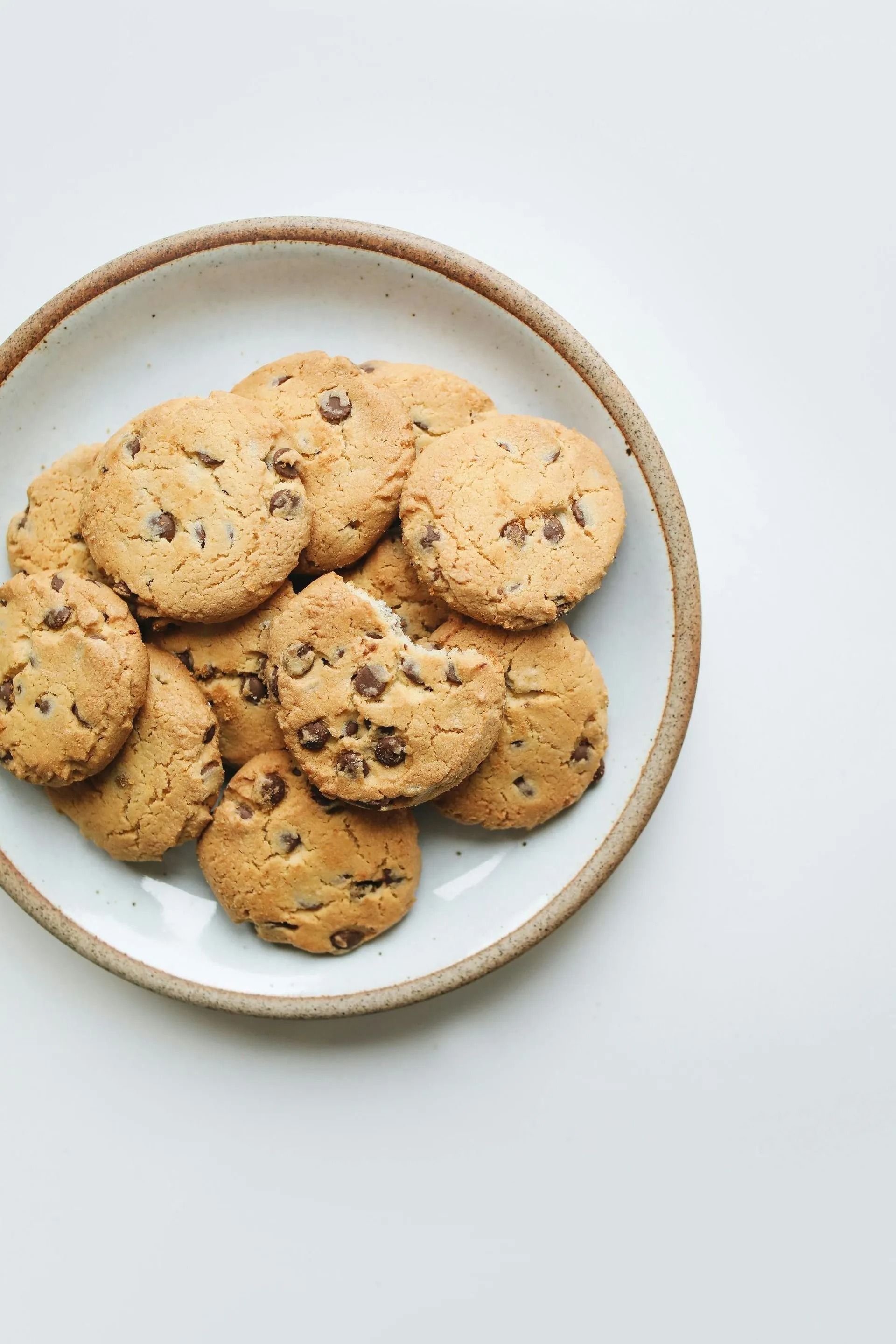 Chocolate chip cookies on a white plate with a brown rim on a white background.