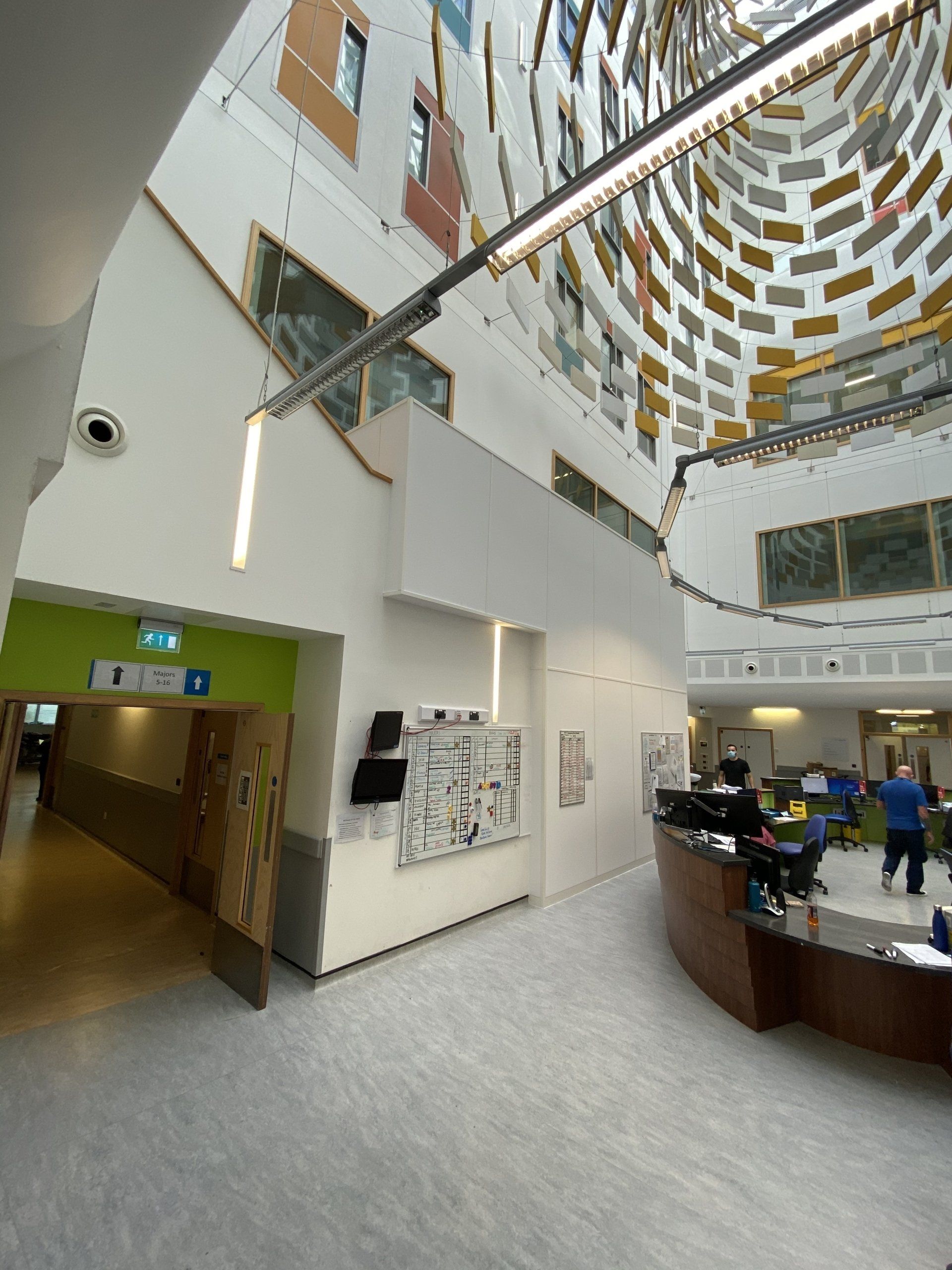 Interior view of a modern hospital with a curved reception desk. White walls, decorative ceiling, and staff visible.