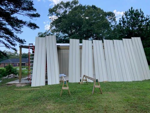A shed is being built in a grassy field with a ladder in the background.