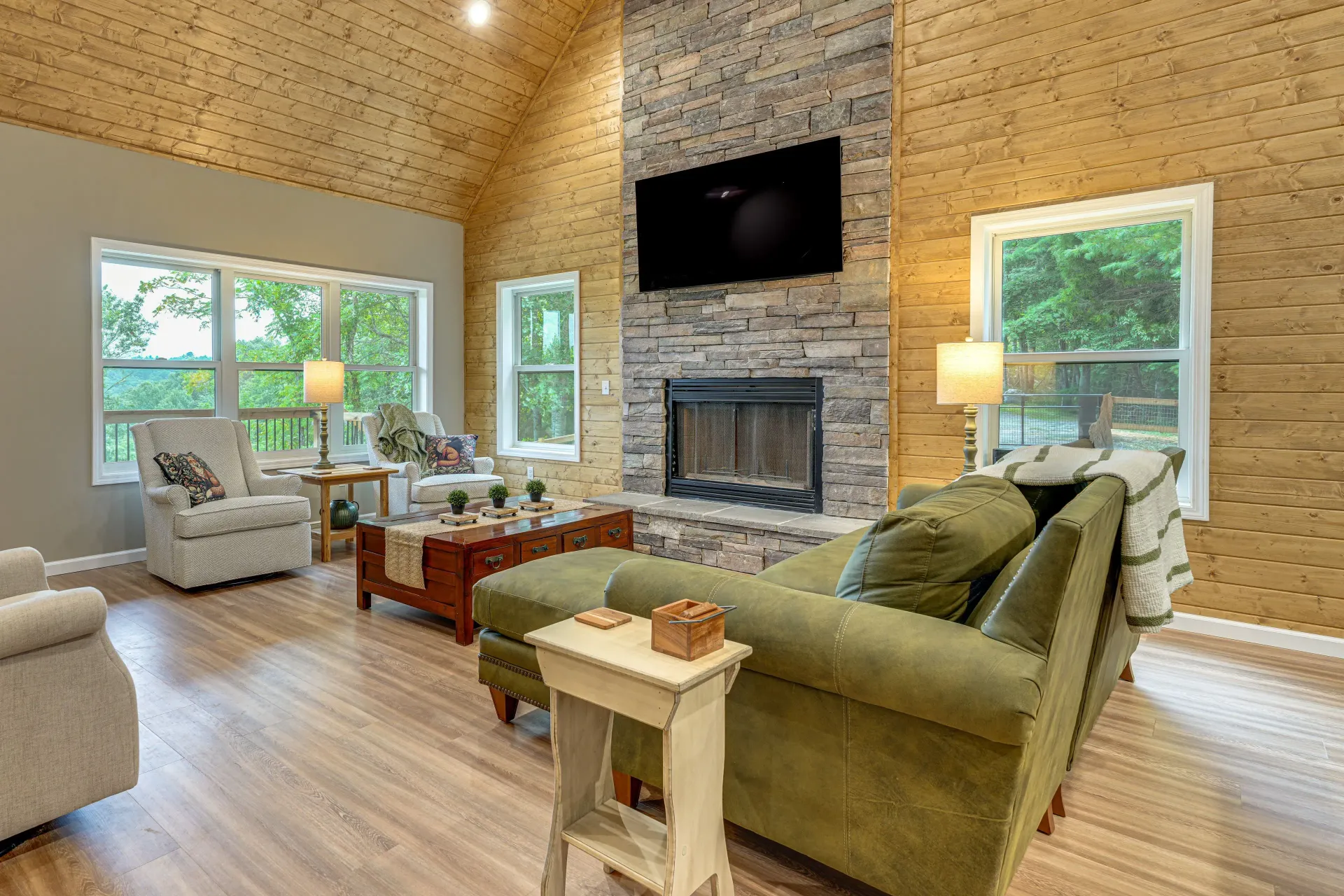 Cozy cabin living room with mountain views, wood beams, sofa, and laptop on a wooden table.