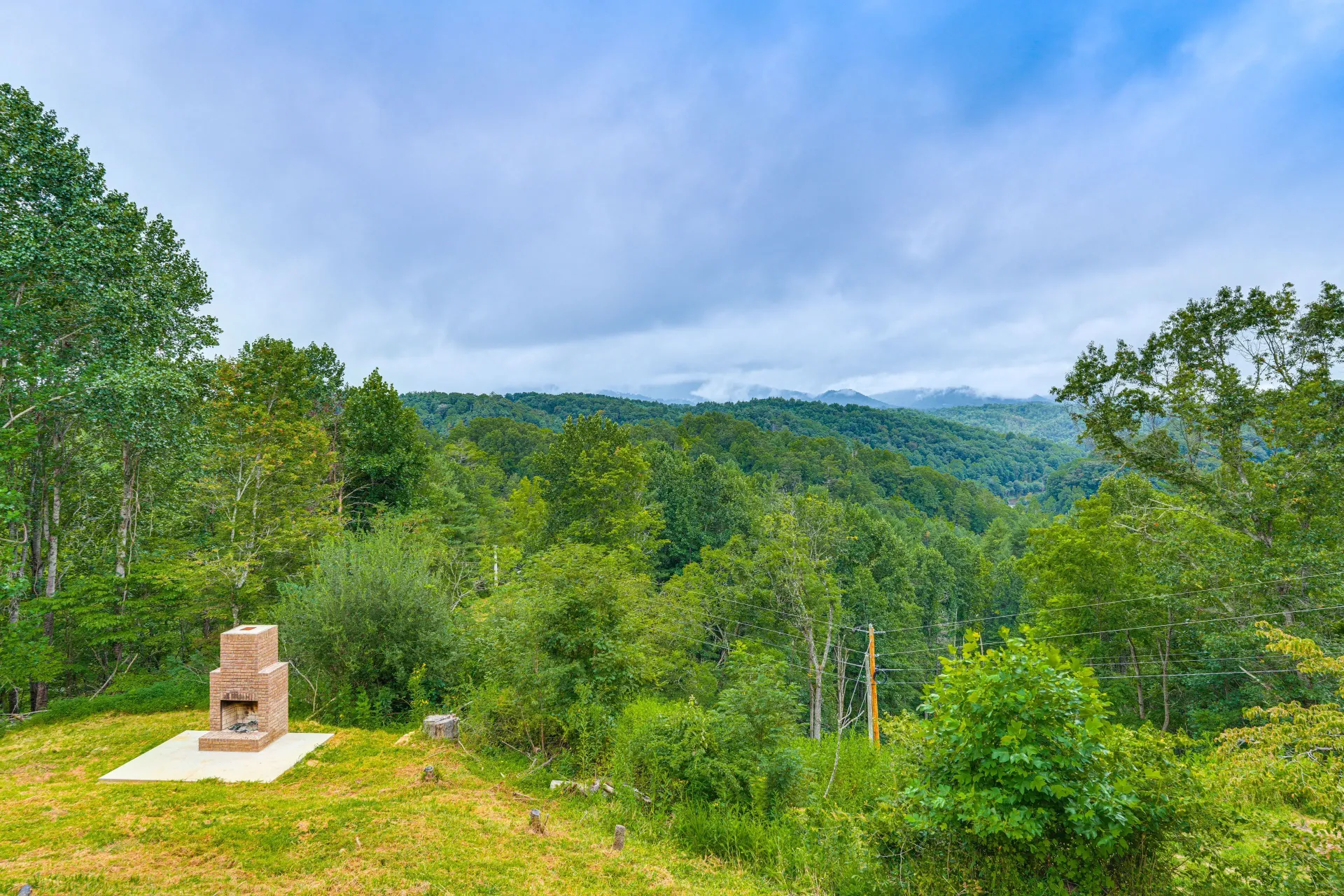 Lush green hillside overlooking a cloudy mountain valley, with a small stone chimney in the foreground