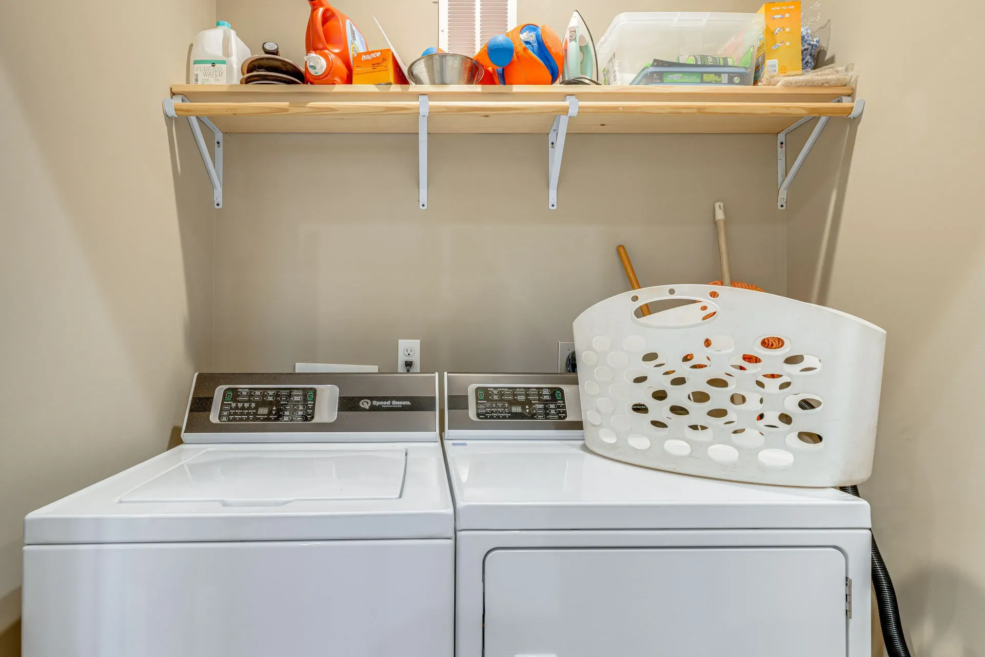 Laundry room with washer, dryer, and a laundry basket on top of the dryer under a shelf