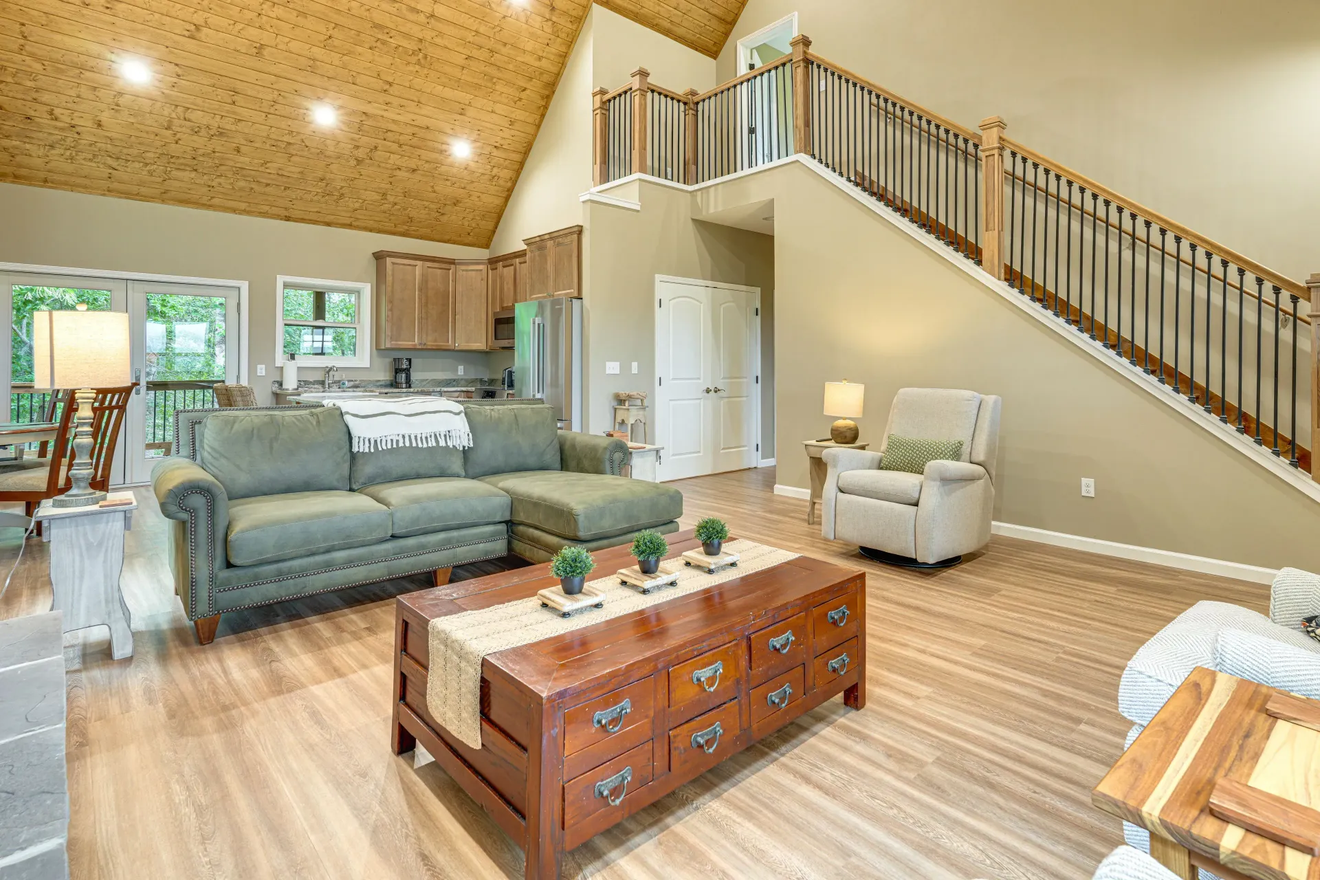 Bright, open living room with gray sofa, wooden coffee table, recliner, and staircase loft.