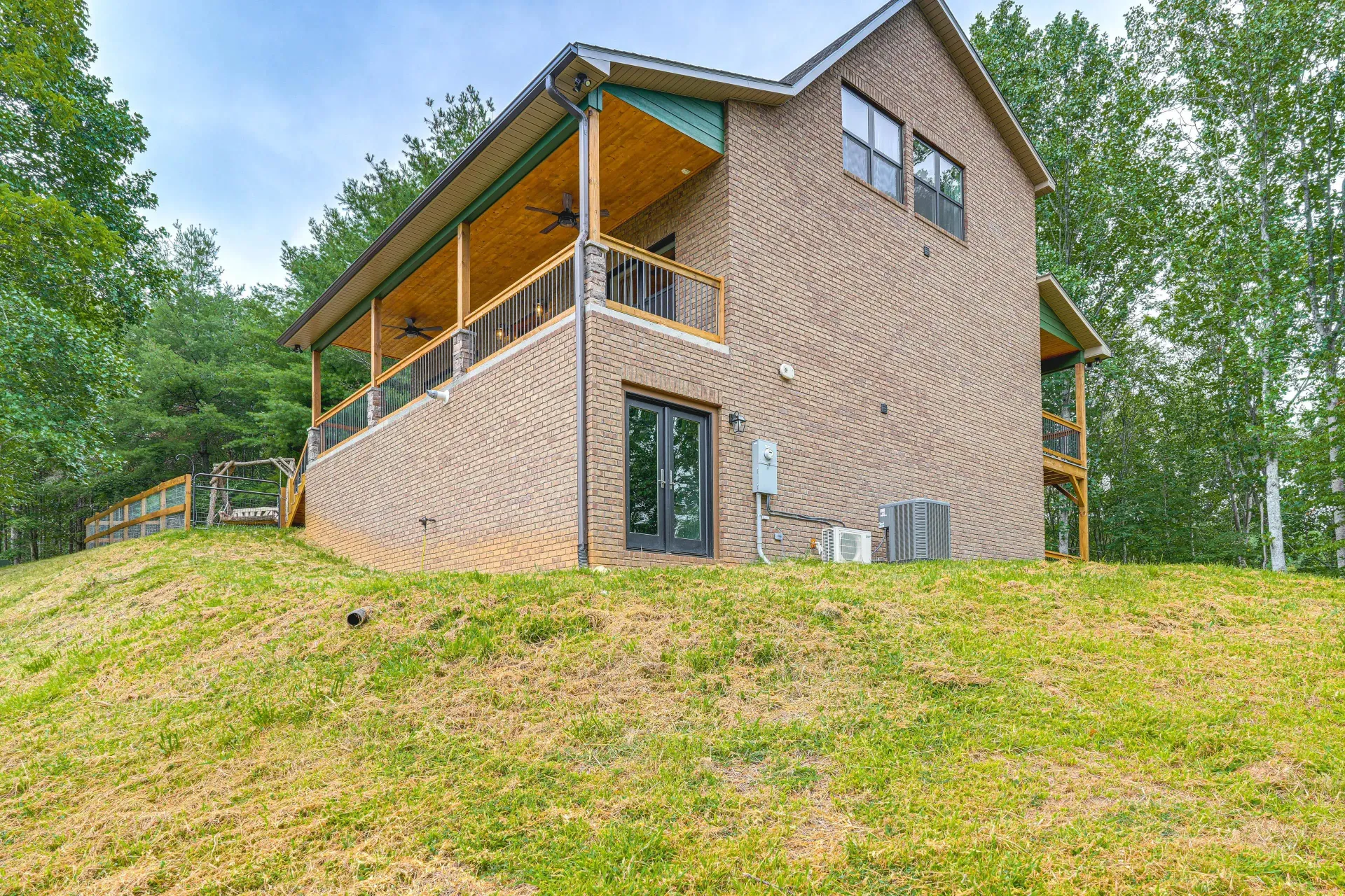 Brick house on a grassy hill with a covered porch and surrounding trees