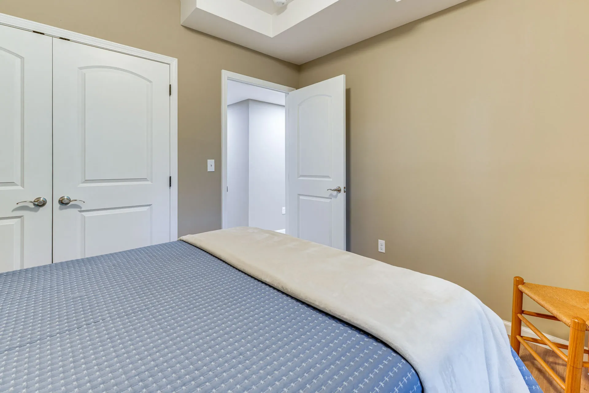 Bright bedroom with blue bedspread, white double doors, open closet door, and beige walls.