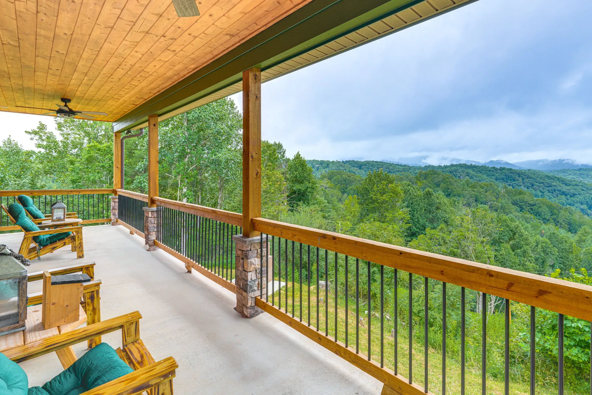 Covered porch with wooden chairs overlooking a green mountain landscape and distant hills