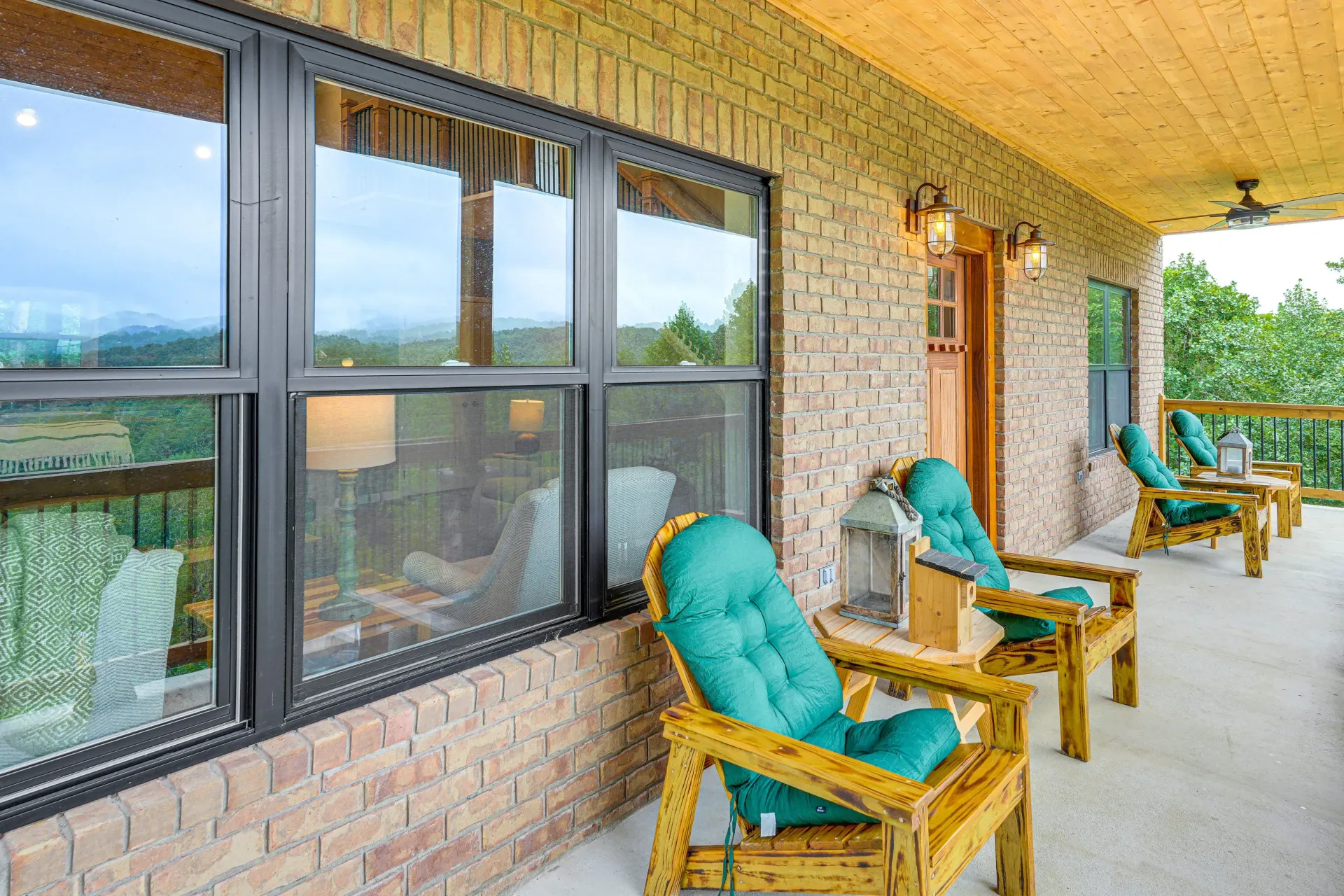 Covered brick porch with turquoise cushioned chairs beside large windows and a wooden door.