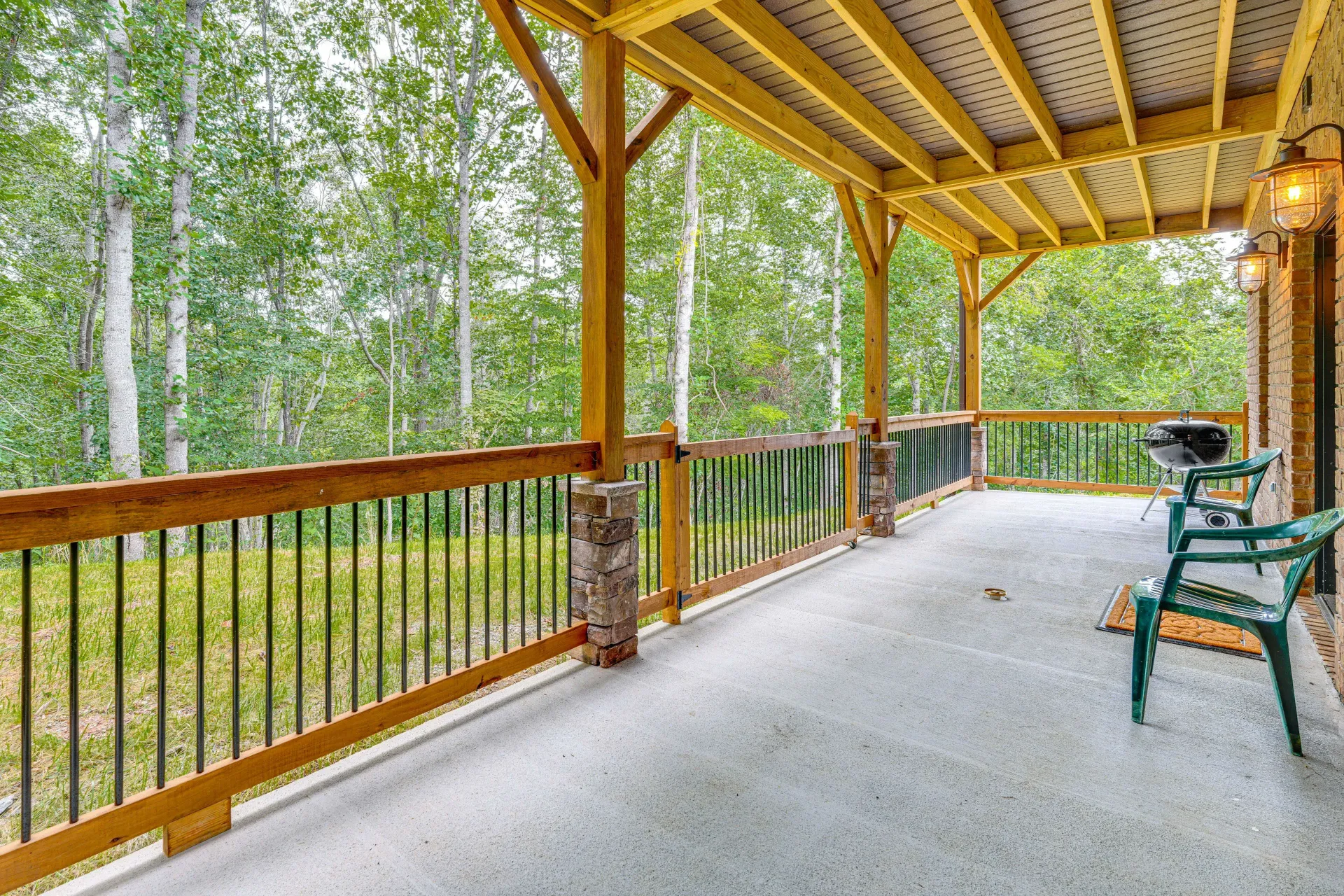 Covered porch with green chairs overlooking a wooded area and wooden railing