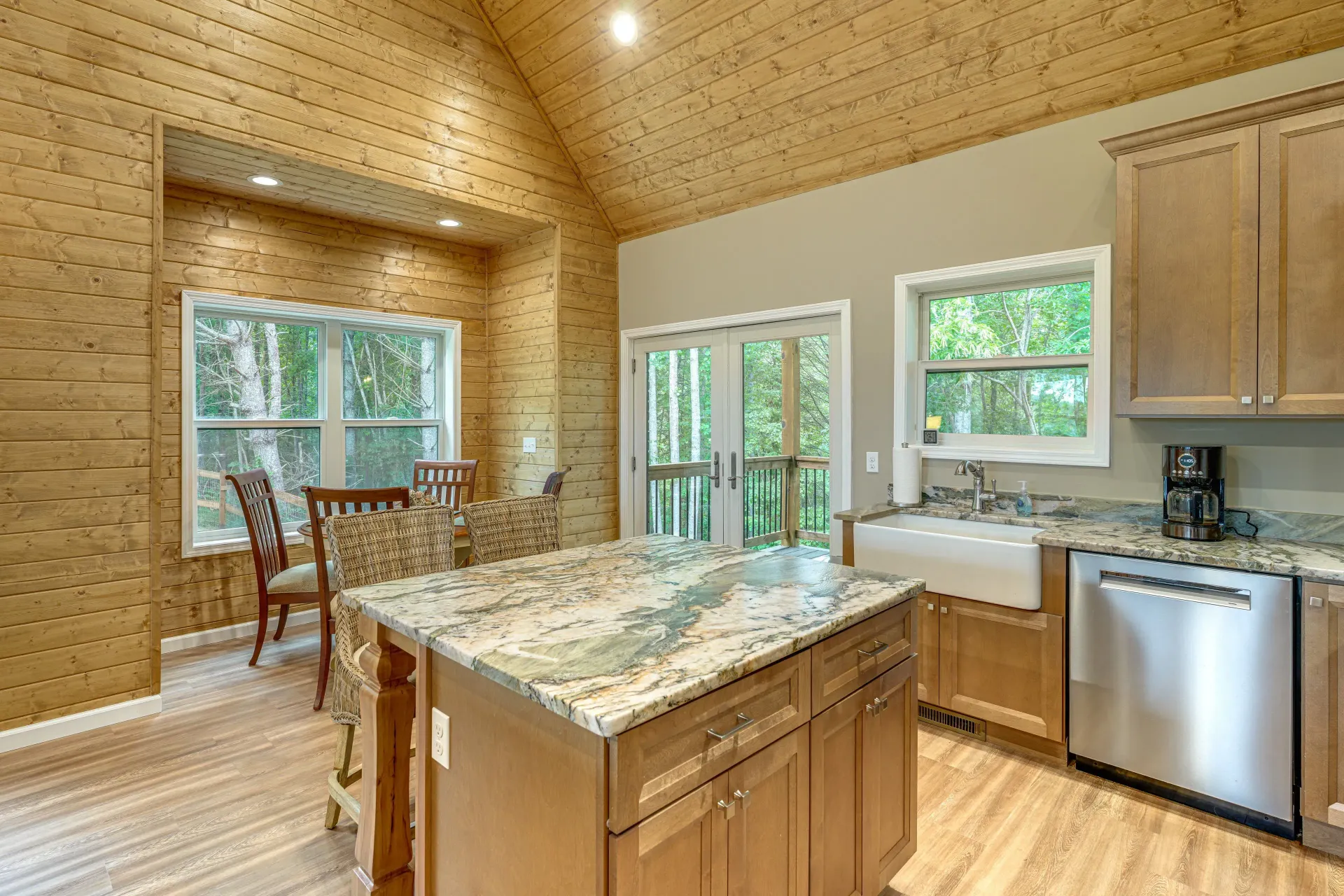 Bright kitchen with wood-paneled walls, granite island, and dining area by large windows