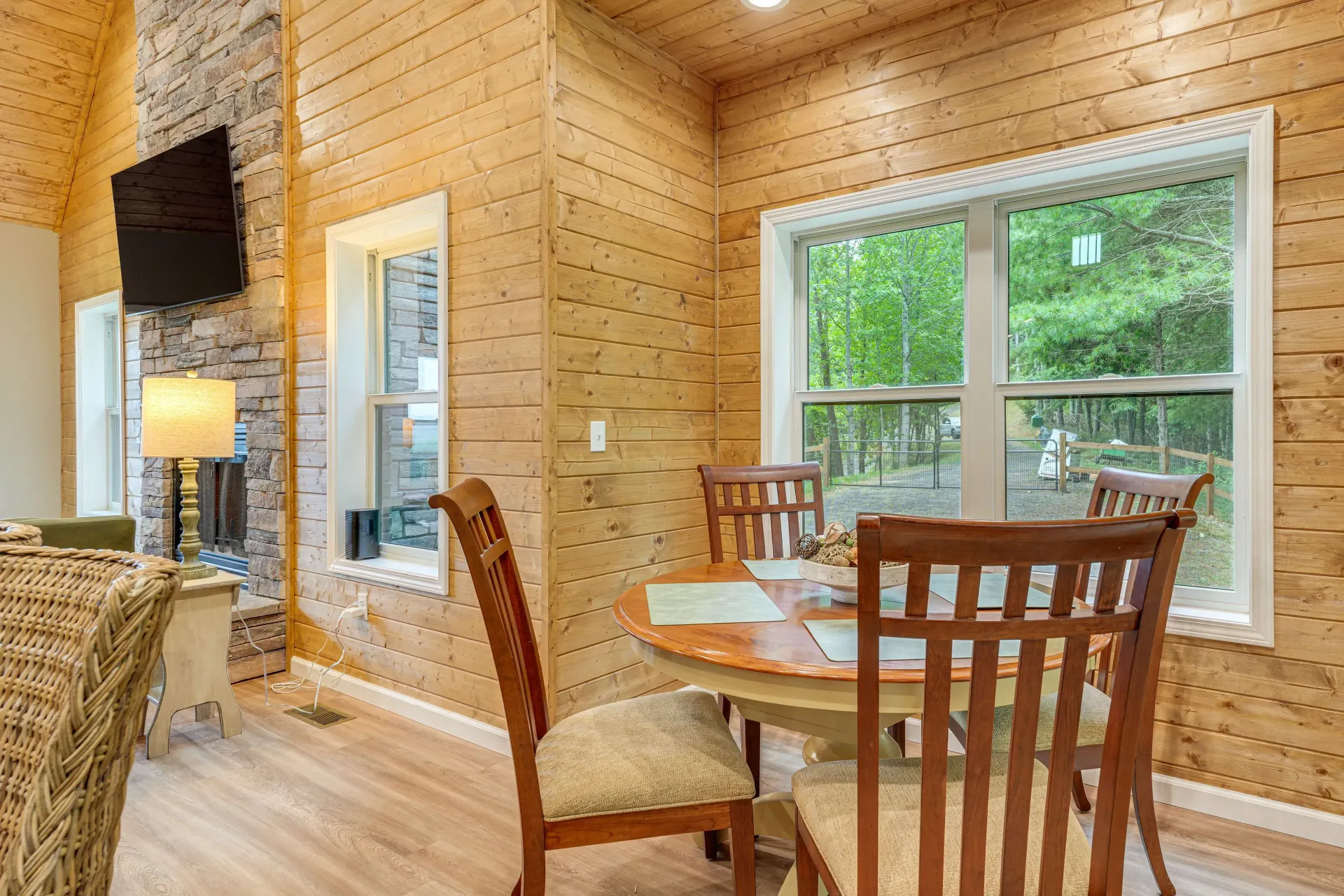 Bright wood-paneled dining nook with table, chairs, lamp, and large window overlooking greenery