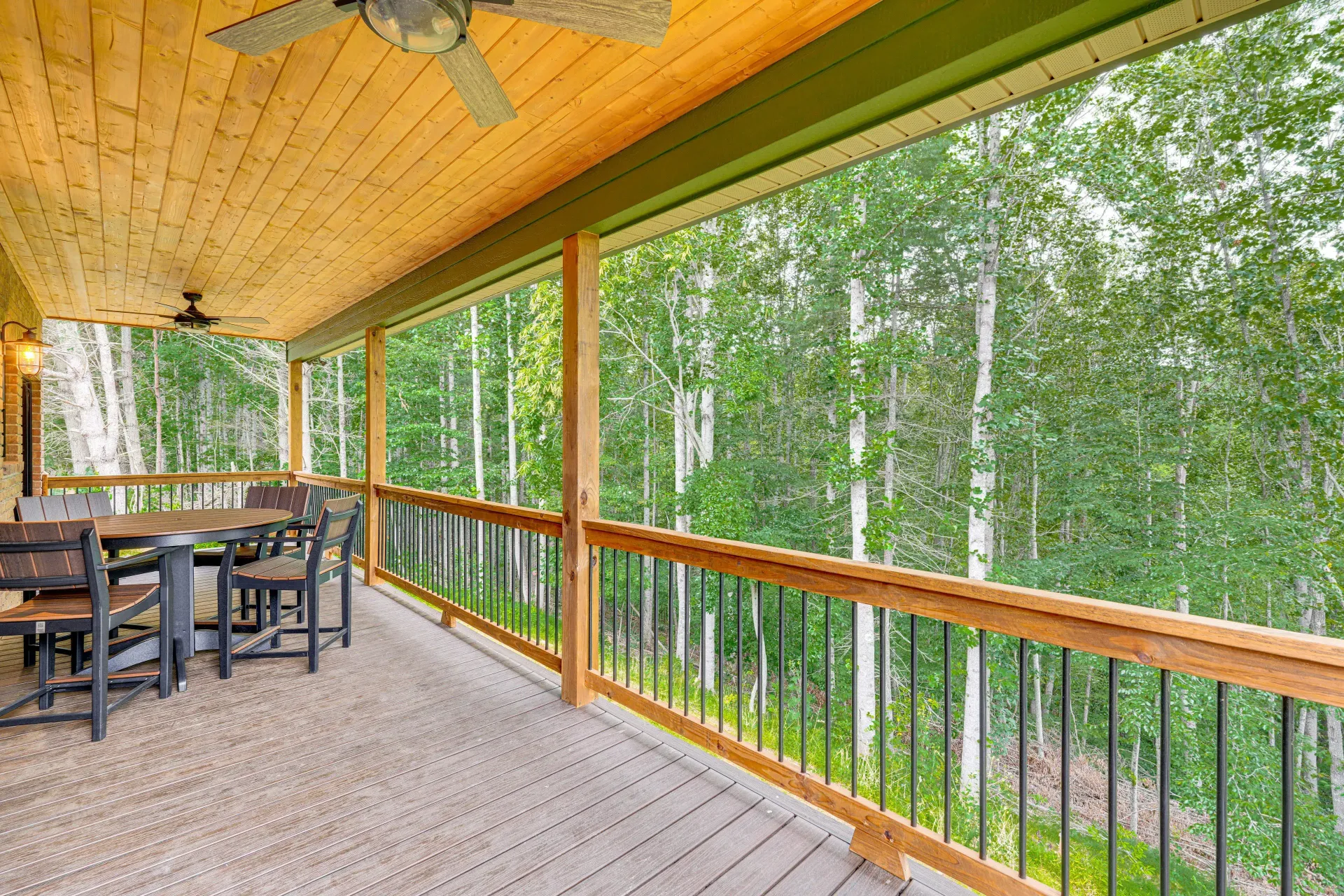 Covered wooden deck with outdoor dining table and chairs, overlooking a wooded forest view
