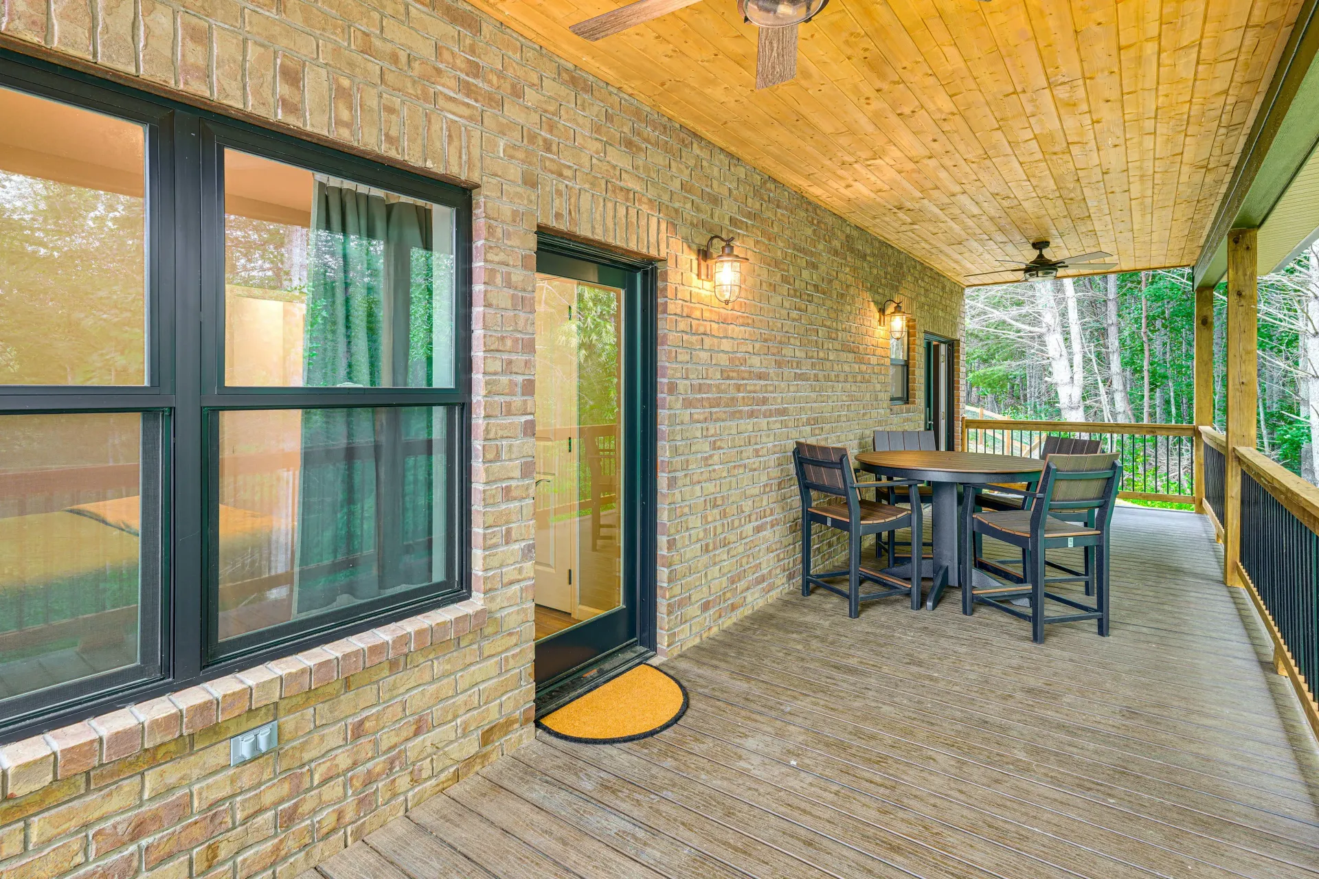 Covered patio with brick walls, ceiling fan, and outdoor dining table overlooking greenery