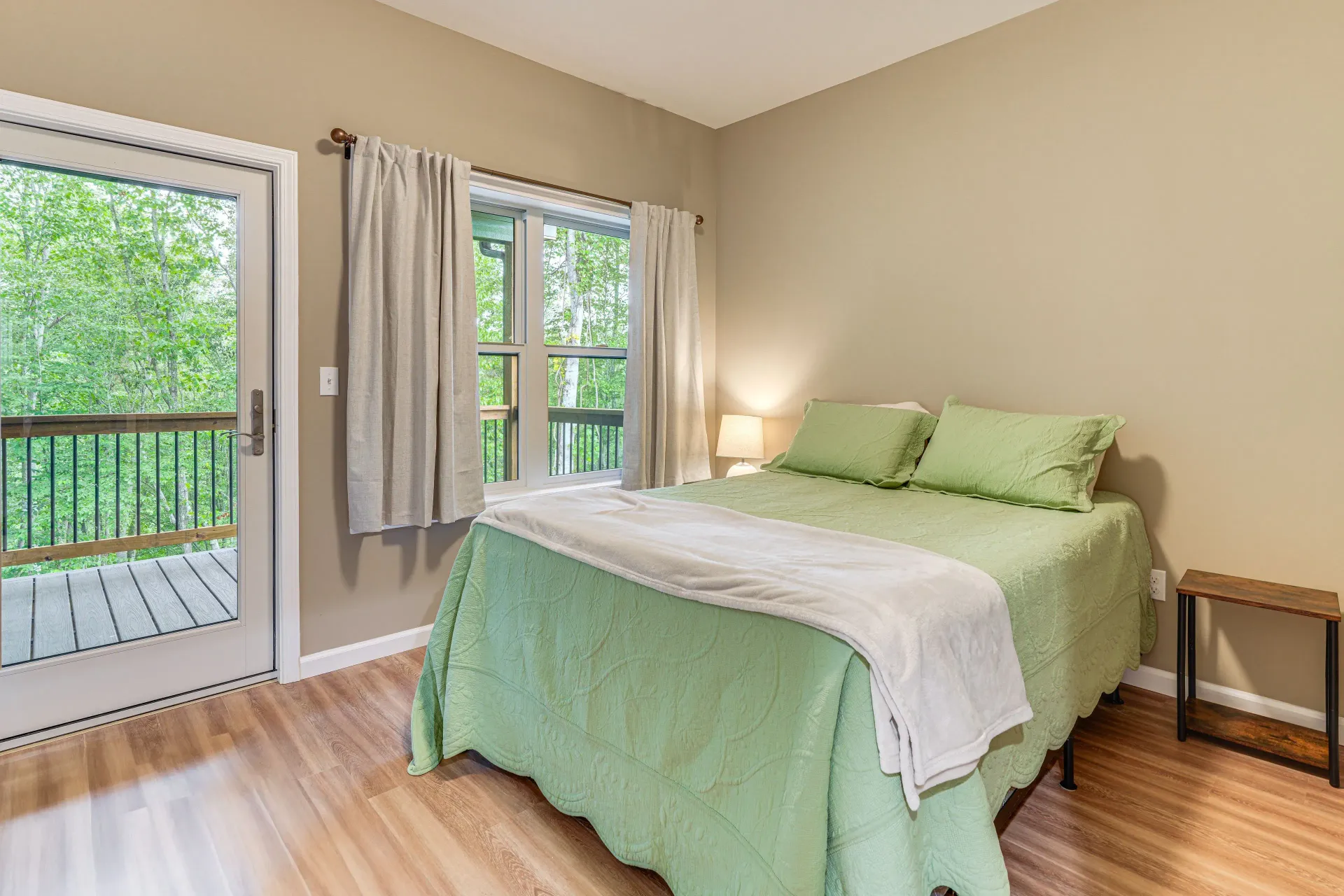 Bright bedroom with green bedspread, wood floors, and sliding glass doors to a balcony