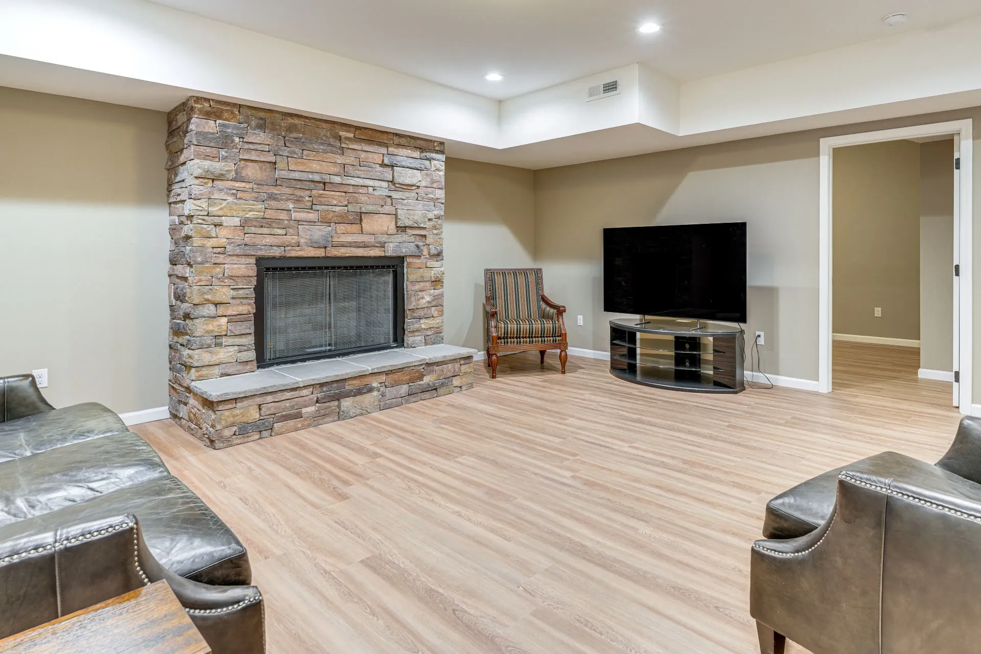 Spacious living room with a stone fireplace, TV, beige carpet, and a few chairs.