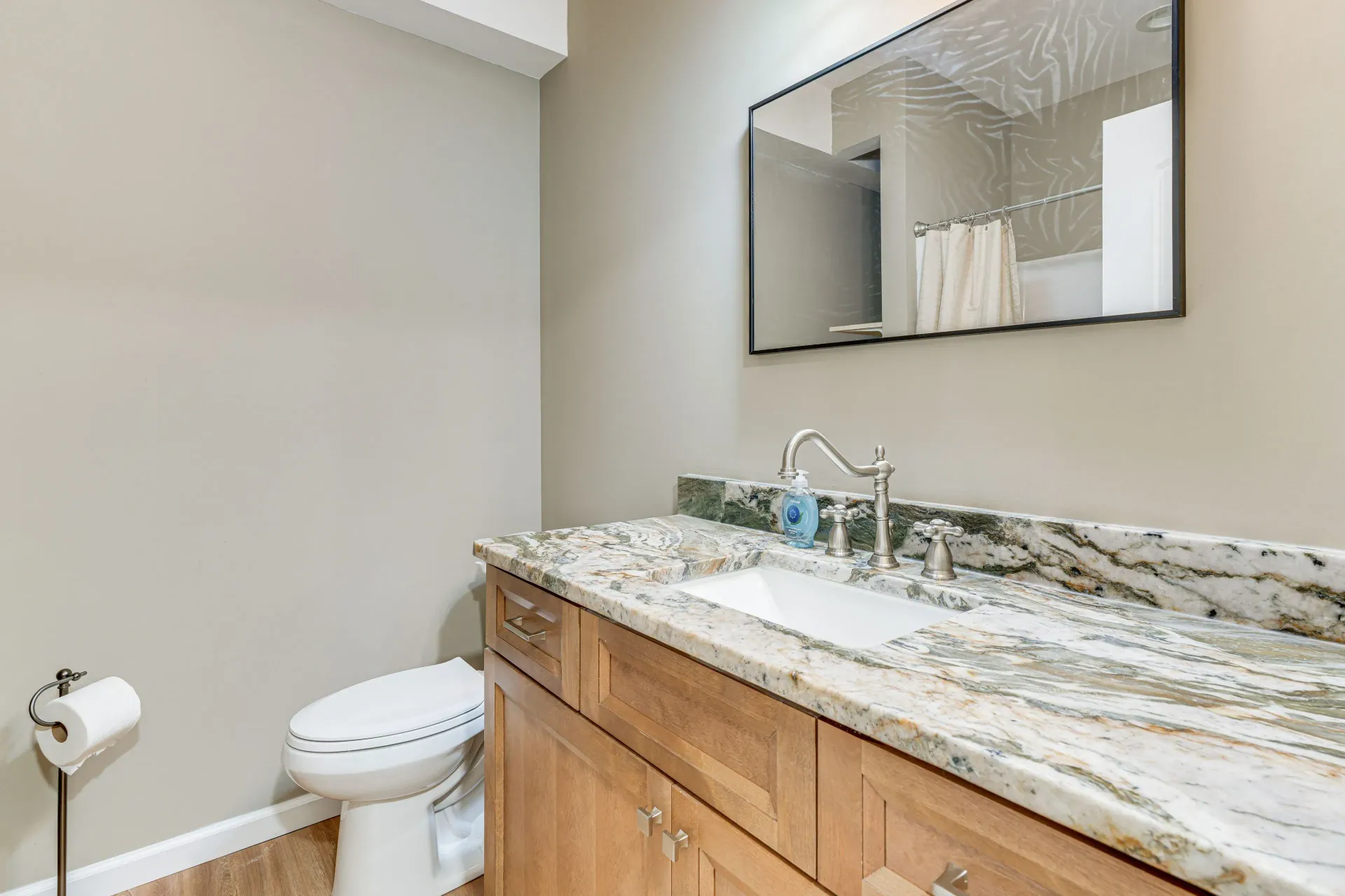 Modern bathroom with wood vanity, granite countertop, sink, mirror, and toilet.