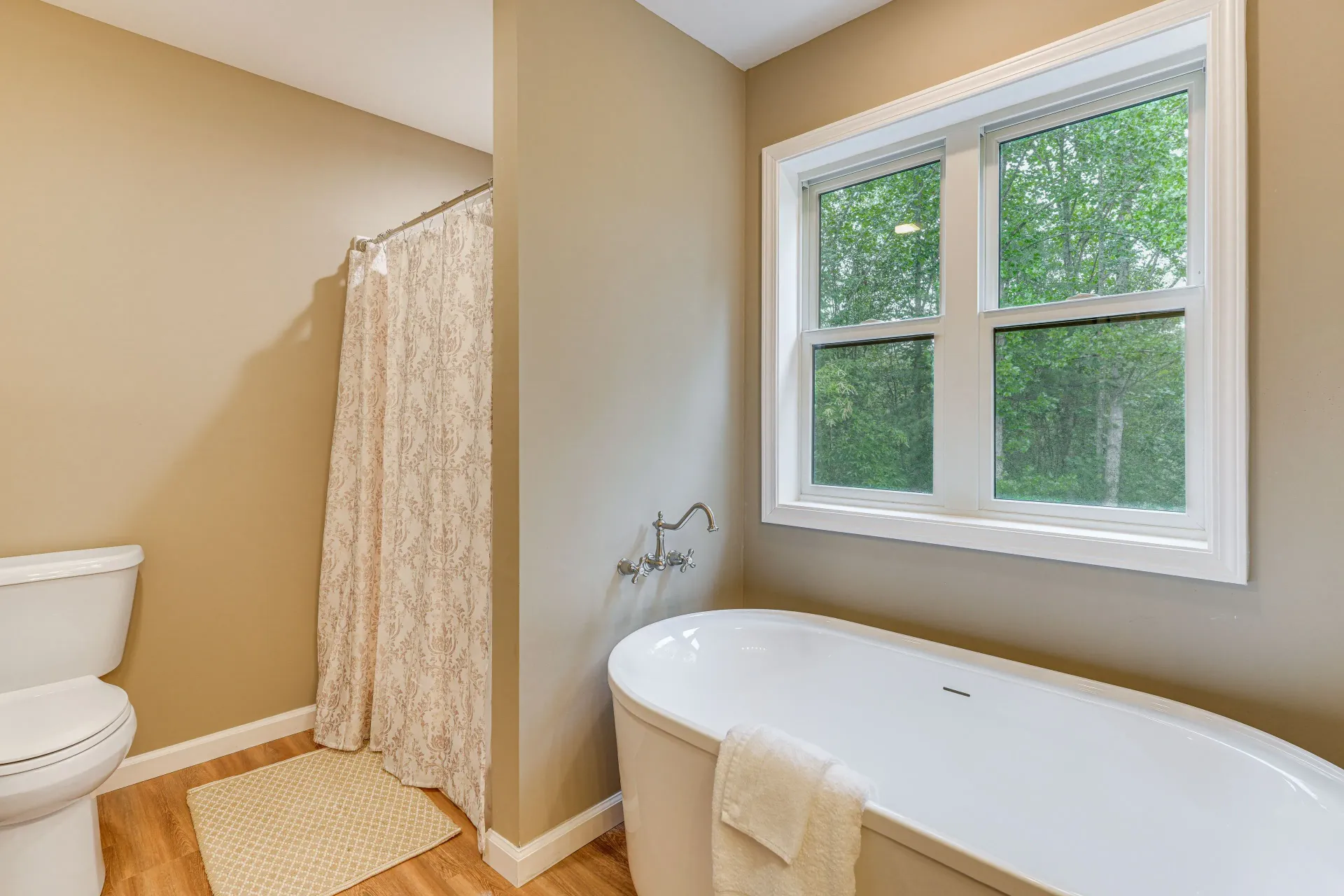 Bright bathroom with a bathtub, toilet, shower curtain, and window overlooking greenery