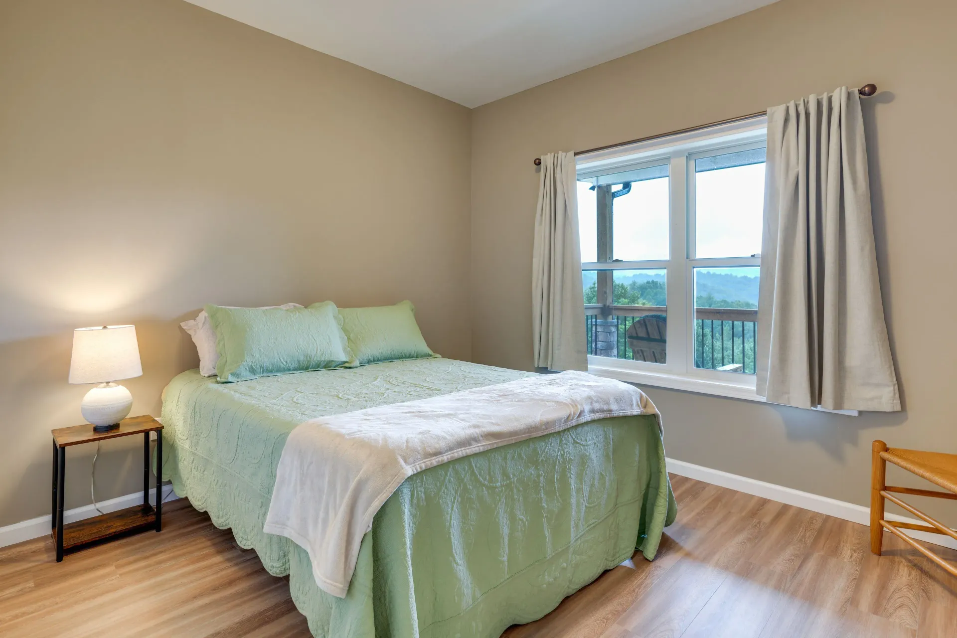 Bright bedroom with a bed, nightstand lamp, window, and light wood floors